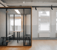 A modern, minimalist room with wooden flooring, large windows, and a glass partition featuring a small table and bench inside.