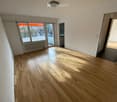 Empty room with wooden flooring, large windows, and a radiator. No furniture or equipment present.