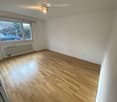 Empty room with wooden flooring, white walls, large window, radiator, and ceiling light fixture.