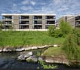 Modern apartment building with multiple floors, balconies, and a grassy area in front