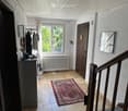 Hallway with tiled floor, staircase, window, coat rack, and small table with items on it.