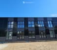 Modern, two-story building with dark, sleek exterior and large windows, featuring a raised ground floor and contemporary design.