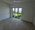 Empty room with tiled floor and large windows offering a view of a green area and water.