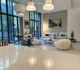 Modern living room with large windows, white sofa, glass coffee table, decorative items, and modern lighting.