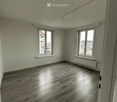 Empty room with light green walls, wooden flooring, and two windows with white frames. No furniture or equipment is present.