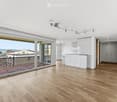 Bright, empty living space with wooden flooring, large sliding glass doors leading to a balcony, white cabinetry, and modern track lighting.