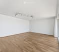 Empty room with white walls, wooden floor, and large windows with white curtains. Track lighting is mounted on the ceiling.