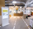 Modern hallway with digital display, reception desk, seating area, and greenery.