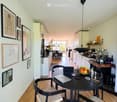 A modern, open-plan kitchen and dining area with light-colored cabinets, a black dining table with four chairs, and various kitchen appliances visible in the background.