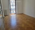 Empty room with wooden herringbone flooring, white walls, and an open door leading to a balcony with a view of a building.