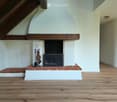 Empty room with wooden flooring and a fireplace with a wooden mantel and brick base. The fireplace includes a black metal grate and a set of fire tools placed beside it.