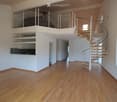 Open, modern hallway with wooden flooring, white walls, a spiral staircase leading to an upper level, and a balcony area visible above.