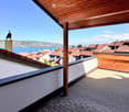 Wooden-roofed balcony overlooking a town with red-tiled roofs and a body of water in the background.