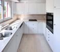 Modern kitchen with white cabinets, stainless steel sink, and built-in oven. Features marble countertops and tiled flooring.