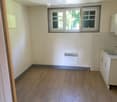 Empty room with wooden flooring, white tiled walls, a window, a radiator, and a small sink with cabinets.