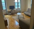 A modern living room with wooden flooring, a sofa, coffee table, desk with a monitor, and a chair.