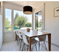 Bright dining area with a wooden table, white chairs, and a bowl of fruit, large windows and sliding doors leading to a balcony.