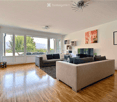 Modern living room with hardwood floors, large windows, grey sectional sofa, coffee table, TV, and decorative artwork.