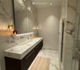 Modern bathroom with marble countertops, a large sink, dark wooden cabinet, and a glass shower enclosure.