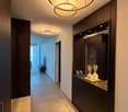 Modern hallway with dark wood paneling, built-in storage, and sleek lighting fixtures. Features a small seating area with a white leather bench and a small table with decorative items.