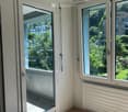 Empty room with wooden flooring, large windows, and a sliding glass door leading to a balcony. The room has white walls and a radiator under the windows.