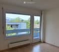 Empty room with wooden flooring, large window, and sliding door leading to a balcony.