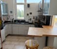 Modern kitchen with stainless steel appliances, white cabinets, a wooden island, and a small seating area with patterned stools.