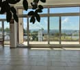 Bright room with large windows and sliding glass doors leading to a balcony, featuring a tiled floor, a small table, and chairs.