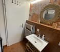 Bathroom with a white sink, mirror, towel rack, and a floral-patterned wall. The floor is tiled, and there is a small wooden shelf under the sink.