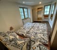 Cozy bedroom with a large bed covered in a patterned duvet, a bedside lamp, a wooden wardrobe, and a chair near the window.