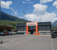 Modern retail building with orange signage, parking lot, and surrounding vineyard landscape with mountains in the background.