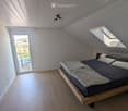 Modern bedroom with wooden floor, slanted ceiling, skylight windows, and a view of the outdoor area.