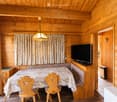Cozy wooden-paneled room with a dining table, chairs, television, and a bench along the wall.