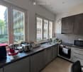 Modern kitchen with grey cabinets, tiled floor, and various appliances including a coffee maker, oven, microwave, and sink.