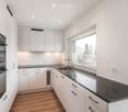 Modern kitchen with white cabinets, dark granite countertop, stainless steel sink and faucet, and built-in oven. Large window provides natural light.