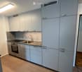Modern kitchen with light grey cabinets, stainless steel sink, faucet, and oven. Light wooden flooring and white walls.