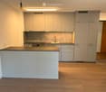 Modern kitchen with light grey cabinets, a central island, and a stainless steel sink.