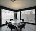 circular white table, 6 black chairs, table lamp, concrete floor, glass walls, exterior view