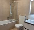 Modern bathroom with beige tiles, a bathtub, toilet, sink, and a glass-enclosed shower area.