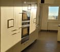 Modern kitchen with light-colored cabinets, built-in oven, tiled floor, and large window providing natural light.