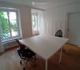 Bright room with wooden flooring, large windows, white table, and black office chair.