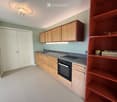 Modern kitchen with wooden cabinets, stainless steel sink, oven, and red shelving unit.