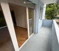 Balcony with wooden floor, glass sliding doors, white railing, and view of greenery.