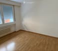 Empty room with wooden flooring, white walls, and large windows with blinds. A radiator is visible under the windows.