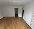 Empty room with light wooden flooring, white walls, and two open doorways leading to other spaces.