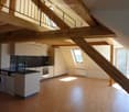 Modern kitchen with white cabinets, black countertops, stainless steel appliances, and wooden flooring. Features a staircase leading to an upper level.