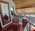 Staircase with wooden railings, red carpet, large mirror, bookshelves, decorative vases, and chandelier visible in the background.