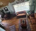 Living room with wooden flooring, two sofas, coffee table, dining area with chairs and table, chandelier, fireplace, and decorative items.