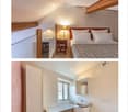 Cozy attic bedroom with wooden beams, a double bed with white pillows and a fur throw, a nightstand with a lamp, and a small table with a mirror.