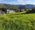 A peaceful garden area with a white house, surrounded by green fields and mountains in the background.